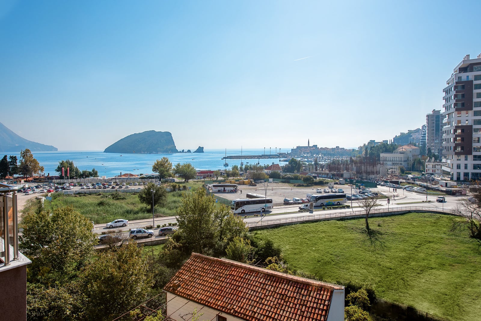 View from the balcony of an apartment in Budva, Montenegro: panorama of the sea, St. Nicholas Island, and city infrastructure.