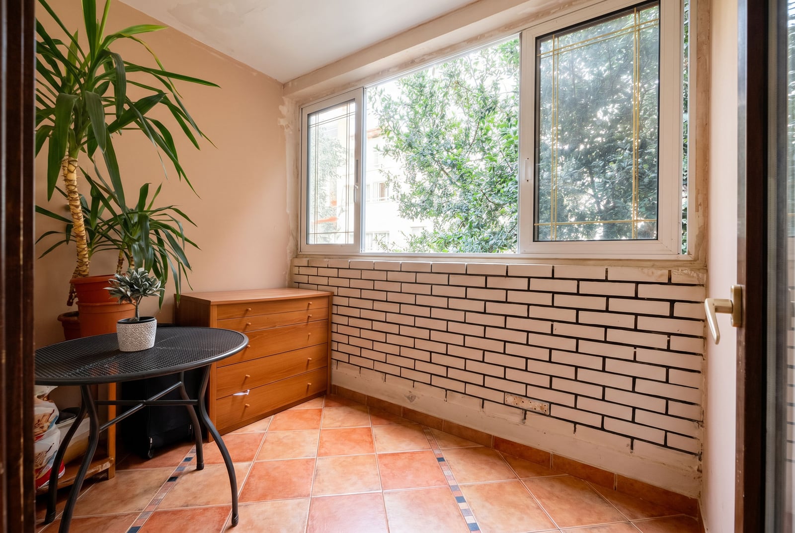Cozy balcony in a Budva apartment, Montenegro: brick wall finish, tiled floor, small table, and house plants.