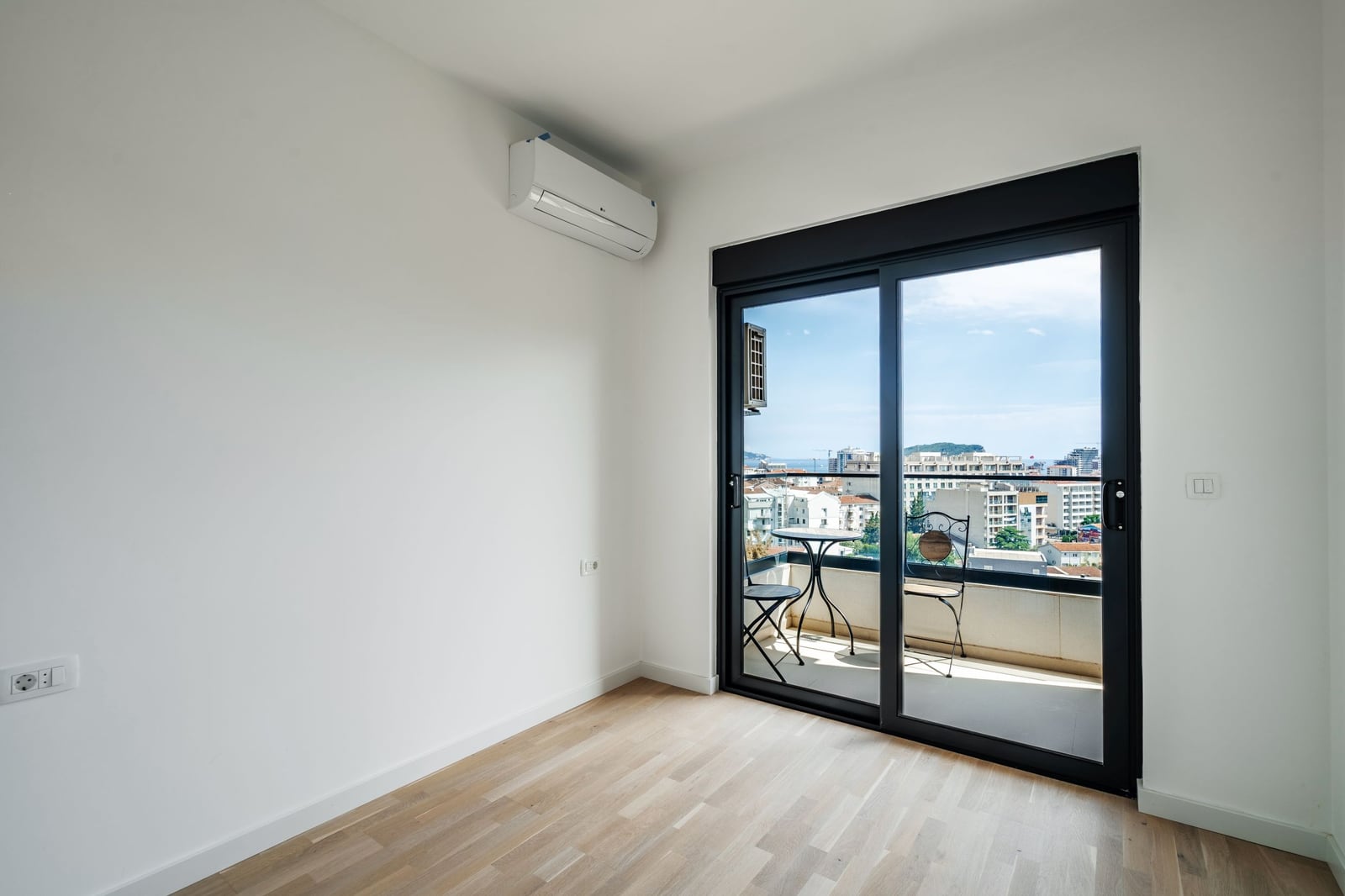Bright bedroom with a panoramic window and access to a balcony in a residential complex, Budva, Montenegro. View of the city and the sea.