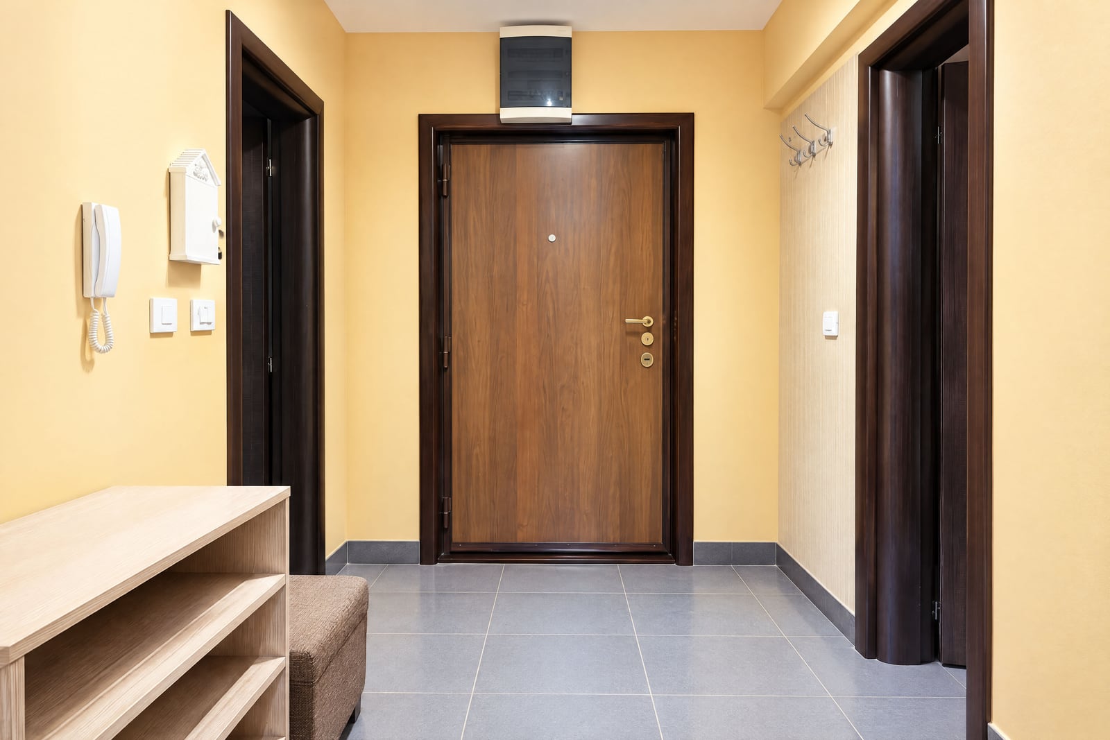 Entryway with a wooden door, wall phone, open shelving unit, coat hooks, and tiled floor.