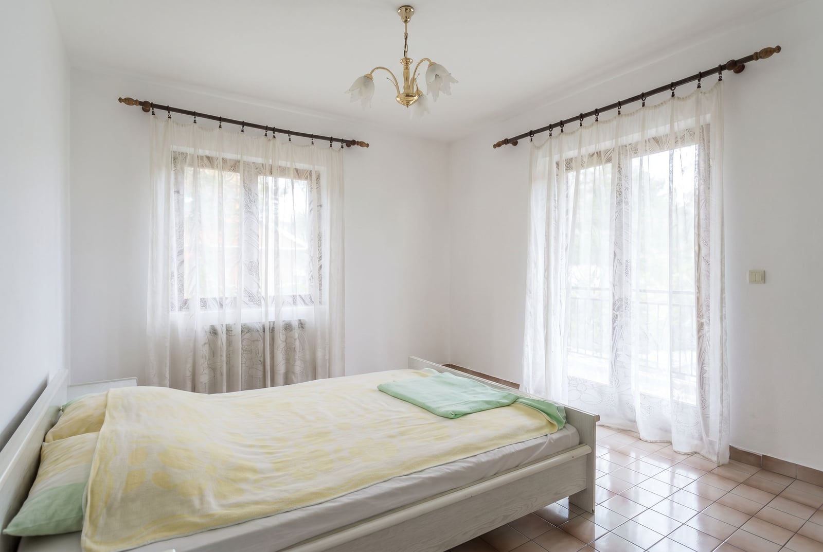 Bright bedroom with a double bed and balcony access in a house, Lastva, Montenegro. Tiled floor, classic decor.