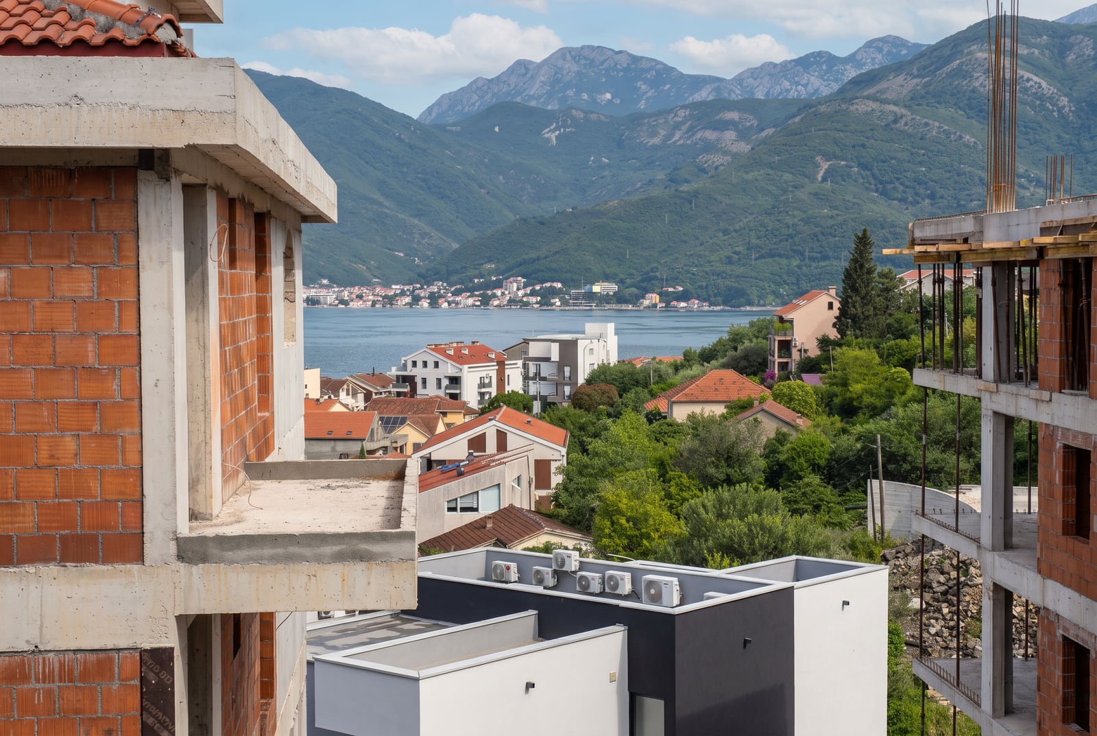 View of a waterfront town and mountains from unfinished brick buildings. Concrete structures in foreground.