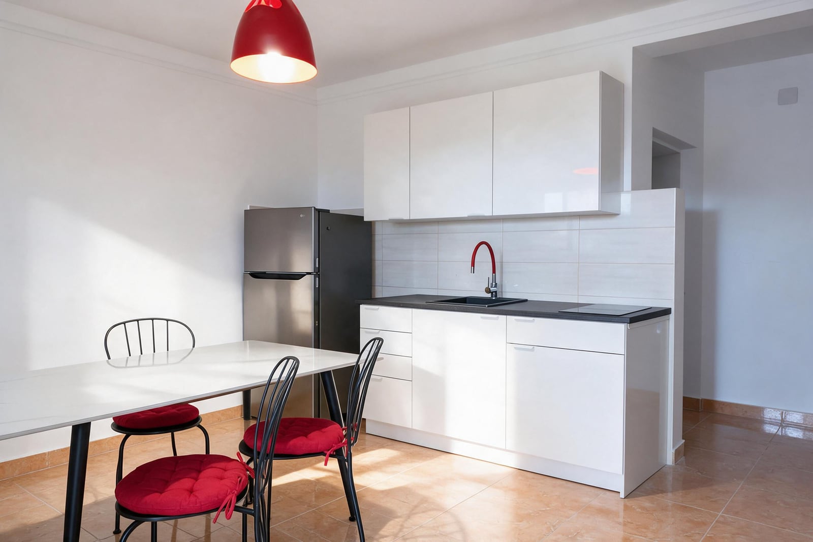 Modern kitchen with white cabinets, black countertop, stainless steel fridge, and dining table with red cushions.