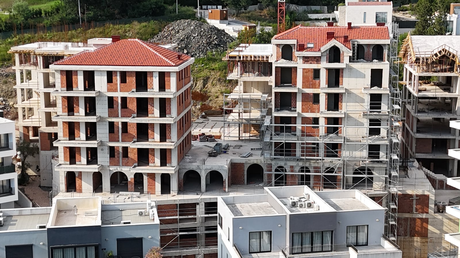Residential buildings under construction with red tiled roofs in Tivat, Montenegro: aerial view of the property.