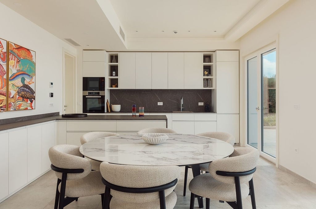 Modern kitchen with a marble table and white cabinetry at a villa in Luštica, Montenegro. Light-toned interior.