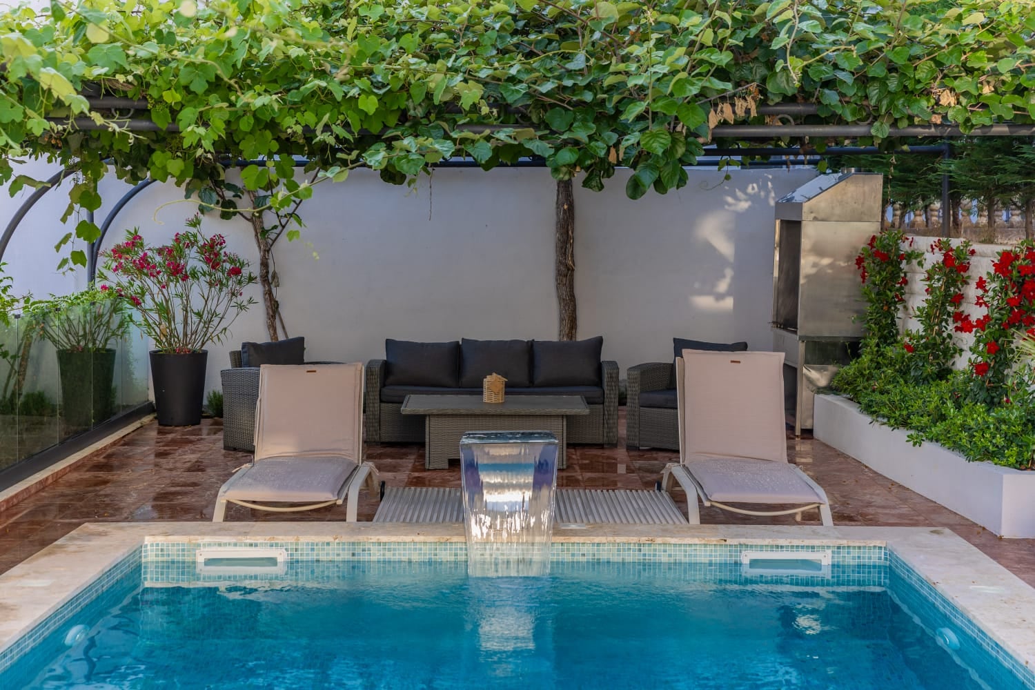 Pool with waterfall and lounge area with sunbeds at a villa in Budva, Montenegro: terrace with garden furniture and barbecue.