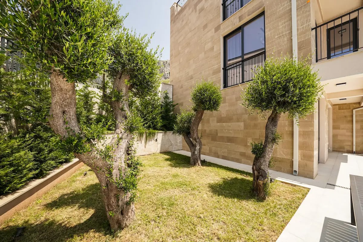 Private garden with olive trees by a stone villa in Reževići, Montenegro. Natural stone facade.