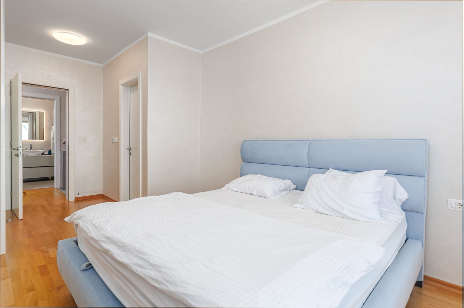 Bright bedroom with a double bed in a penthouse, Becici, Montenegro. View of the bathroom, parquet flooring.