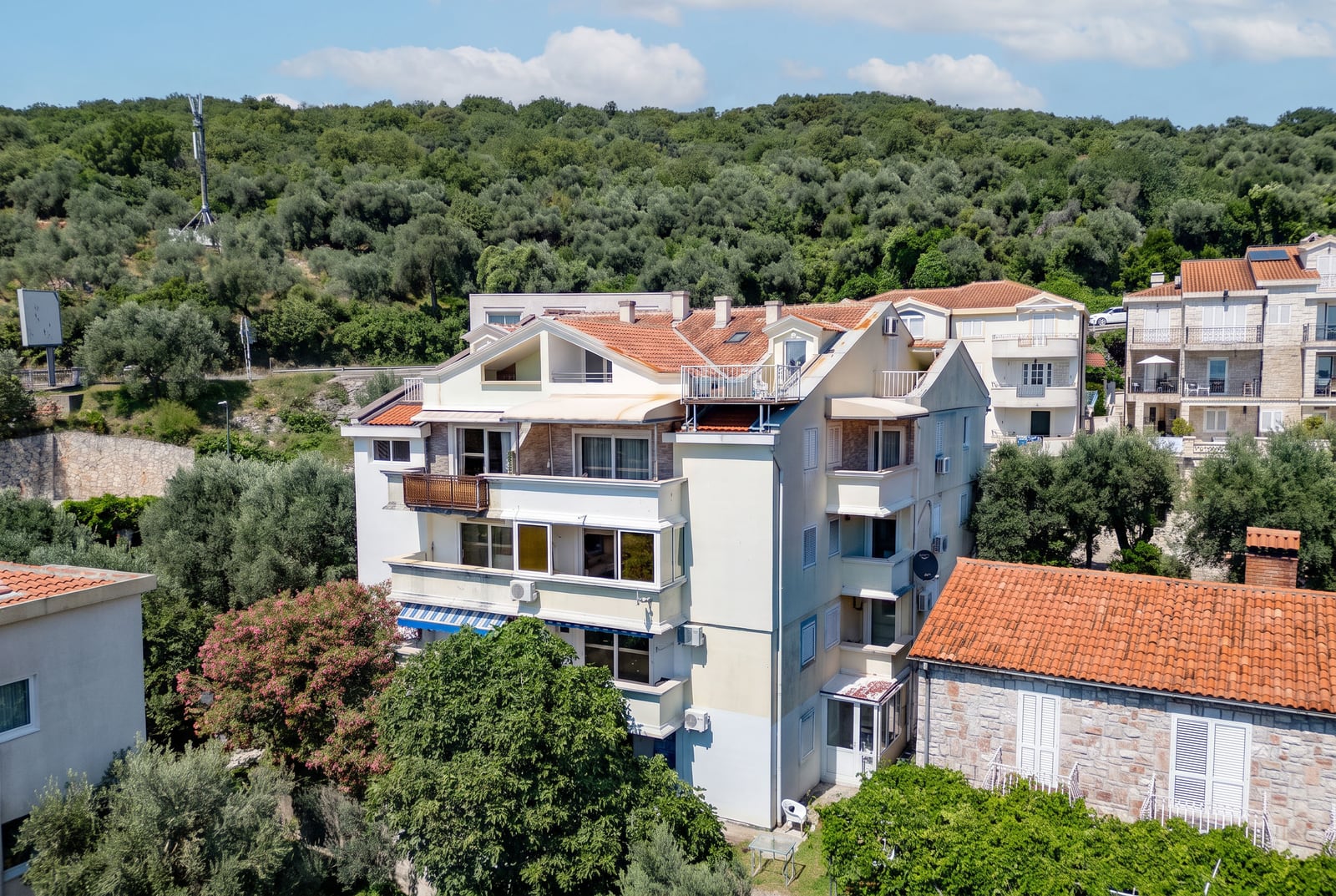 Residential building with terraces and a tiled roof surrounded by greenery, Sveti Stefan, Montenegro — view of the property.