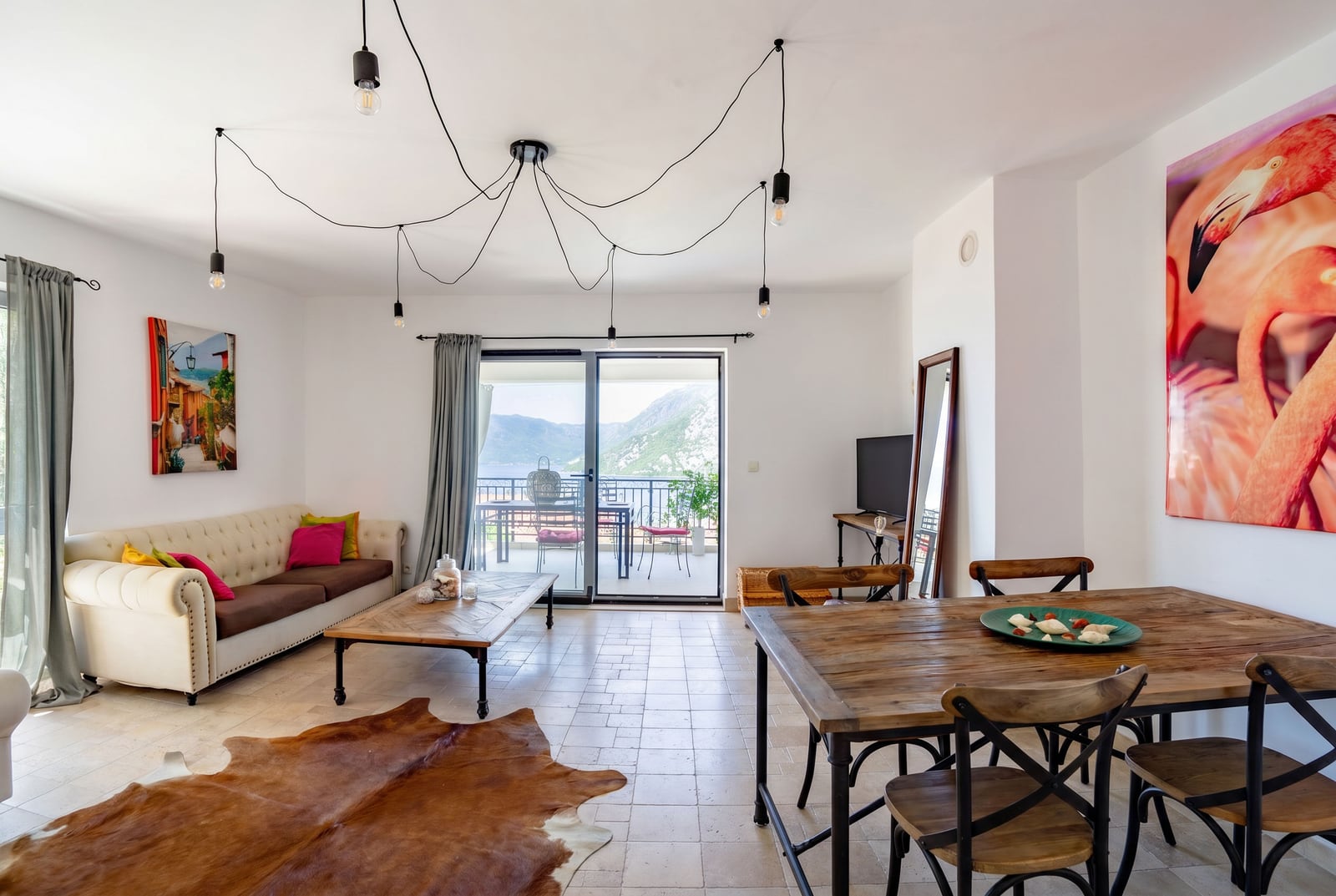 Living room in an apartment in Risan, Montenegro: bright interior, wooden table, sofa, and terrace with a view of the mountains and sea.