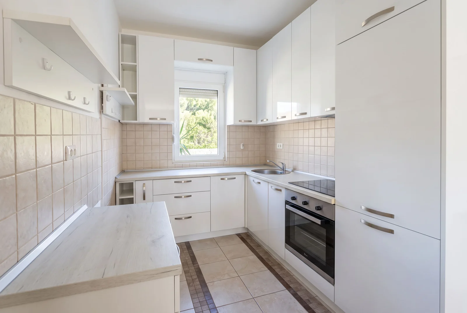 Modern kitchen with white cabinets, tiled walls, built-in oven, sink under a window, and a central island.