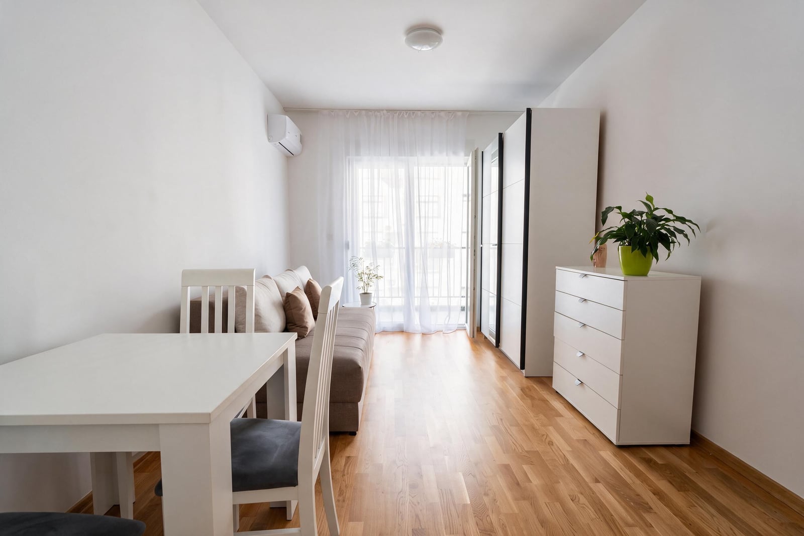 Living room with white dining table, sofa, wardrobe, and wooden flooring.