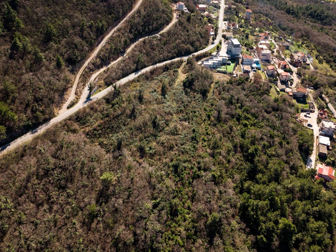Aerial view of a land plot for development in Kotor, Montenegro, with an access road and forest landscape.