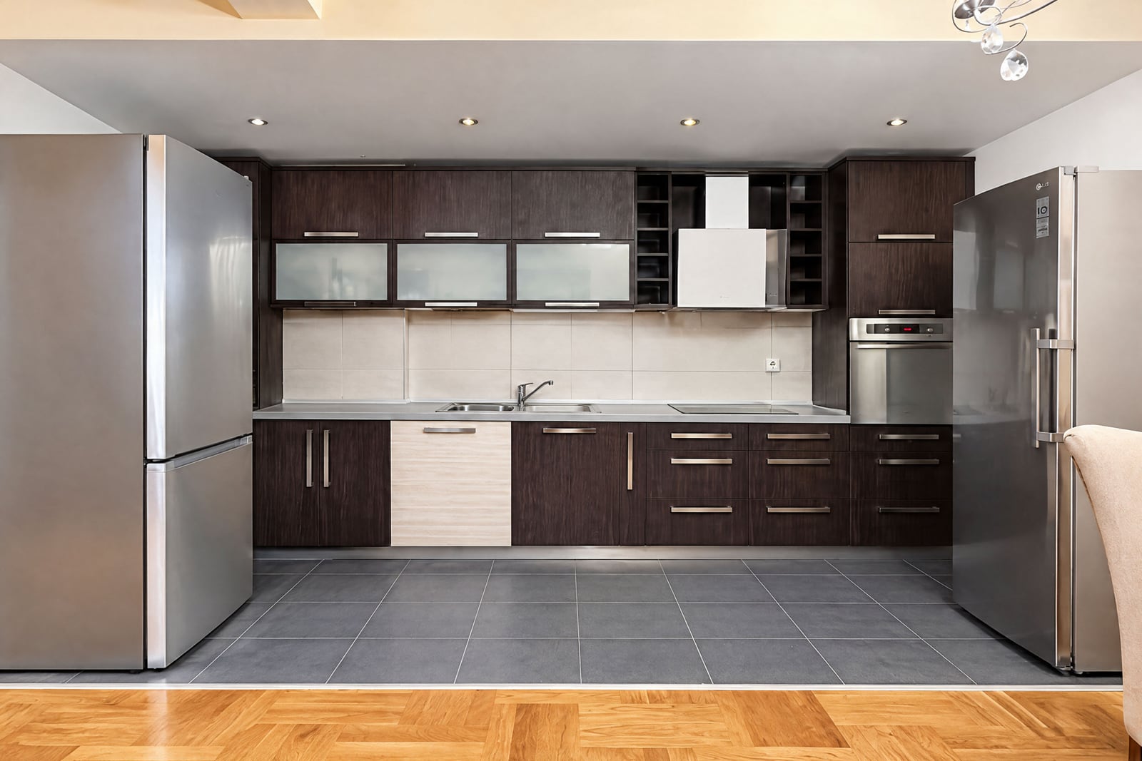 Modern kitchen featuring dark wood cabinets, two stainless steel refrigerators, a sink, and built-in appliances.