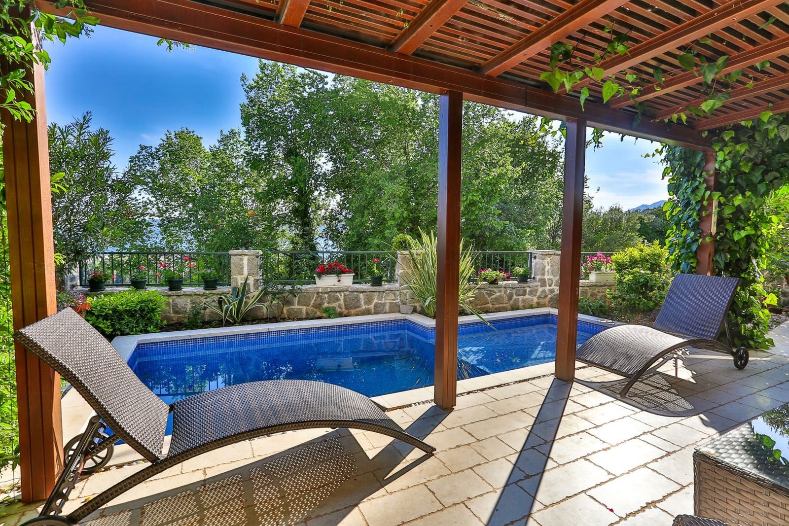 Terrace with a pool and sun loungers at a villa in Tivat, Montenegro: view of the garden, stone finish, and wooden canopy.