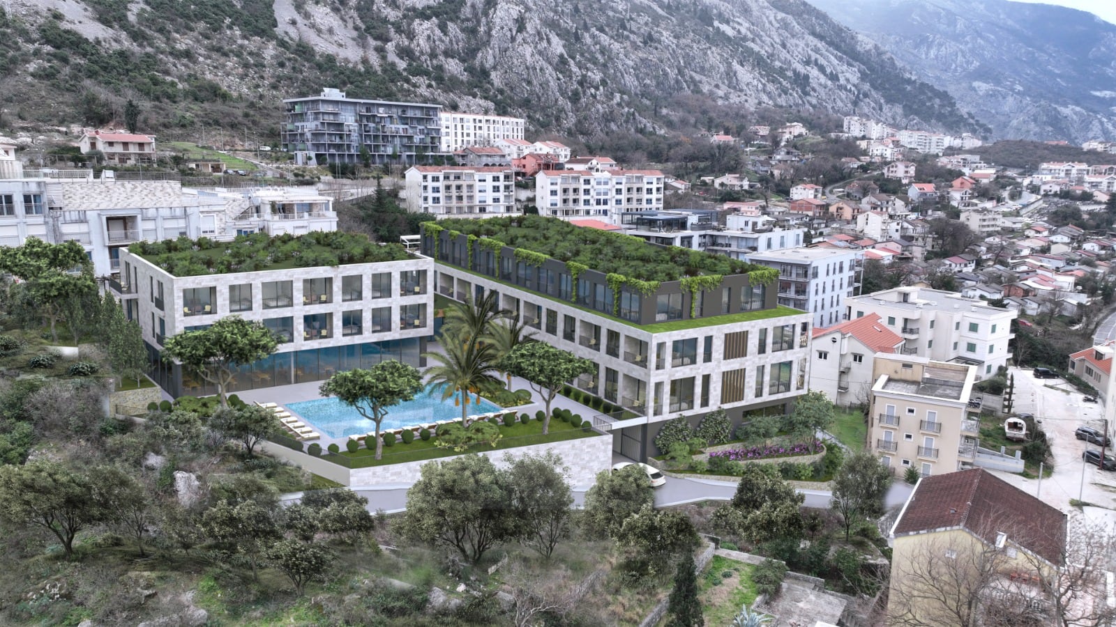 Aerial view of a modern building with a green roof and pool, set against mountains and urban surroundings.