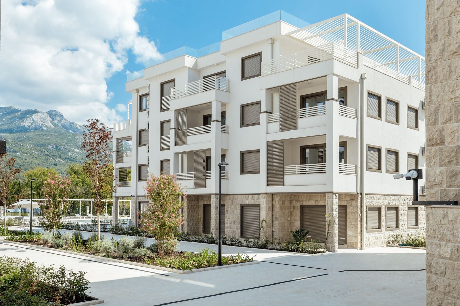 Modern residential complex with terraces and stone finishes in Igalo, Montenegro, set against mountain landscapes.