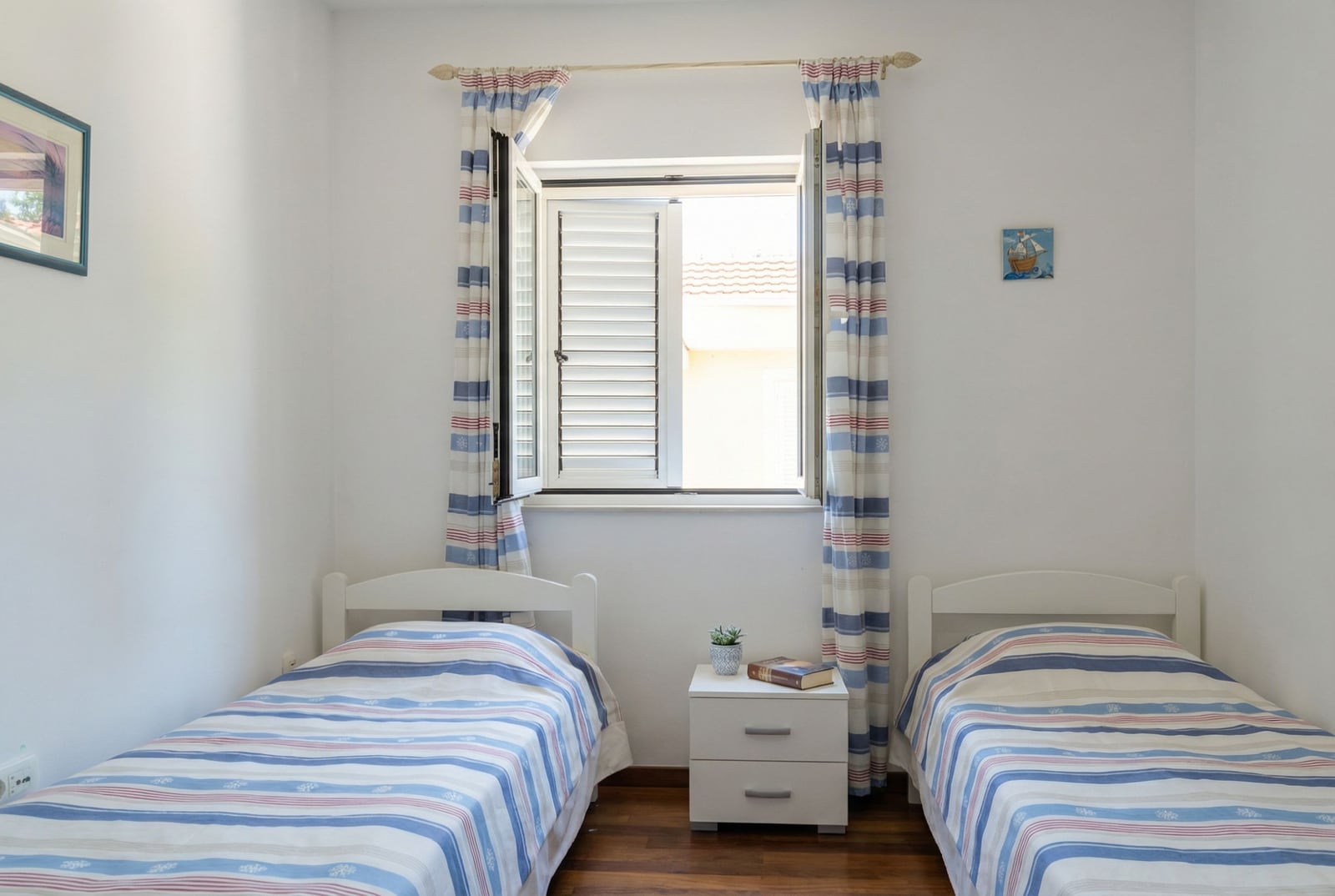 Bright bedroom with two beds in an apartment in Tivat, Montenegro, with a window and traditional shutters.