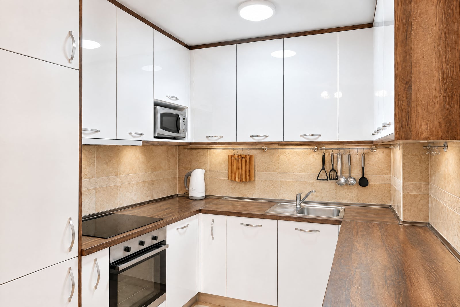 Modern kitchen featuring glossy white cabinets, wood countertops, built-in oven, microwave, sink, and hanging cooking utensils.