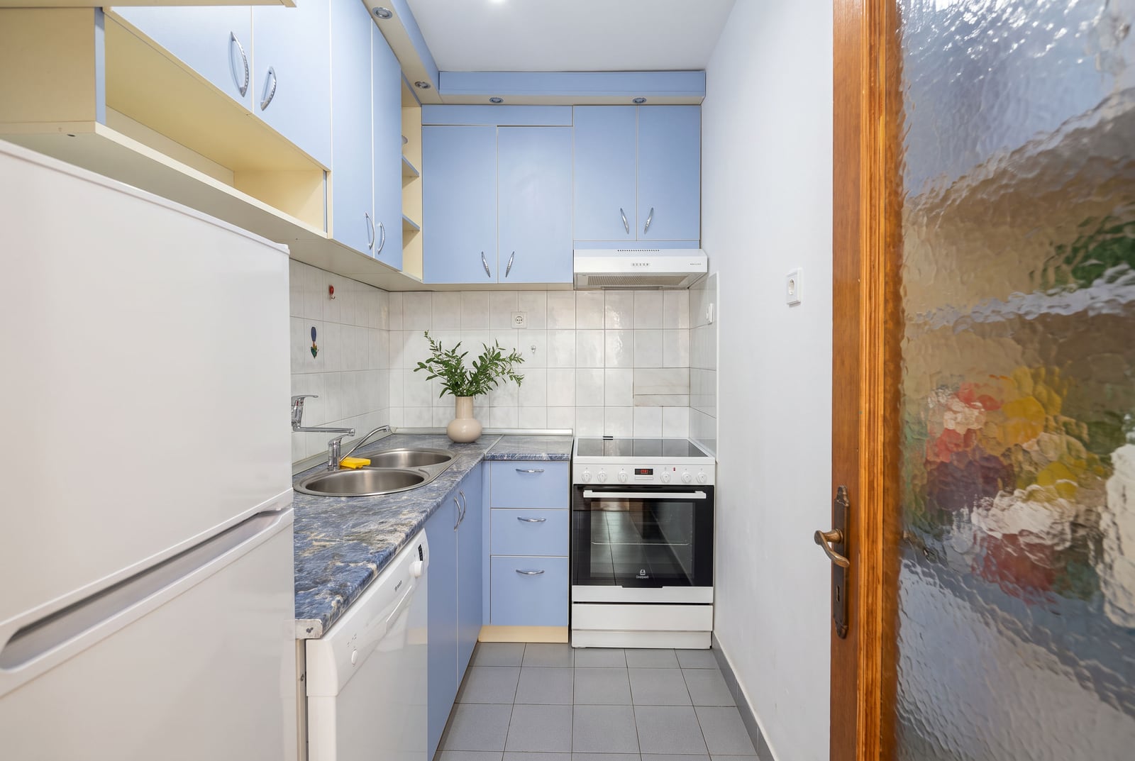 Kitchen with blue cabinets, white appliances, double sink, and stove on a stone countertop.