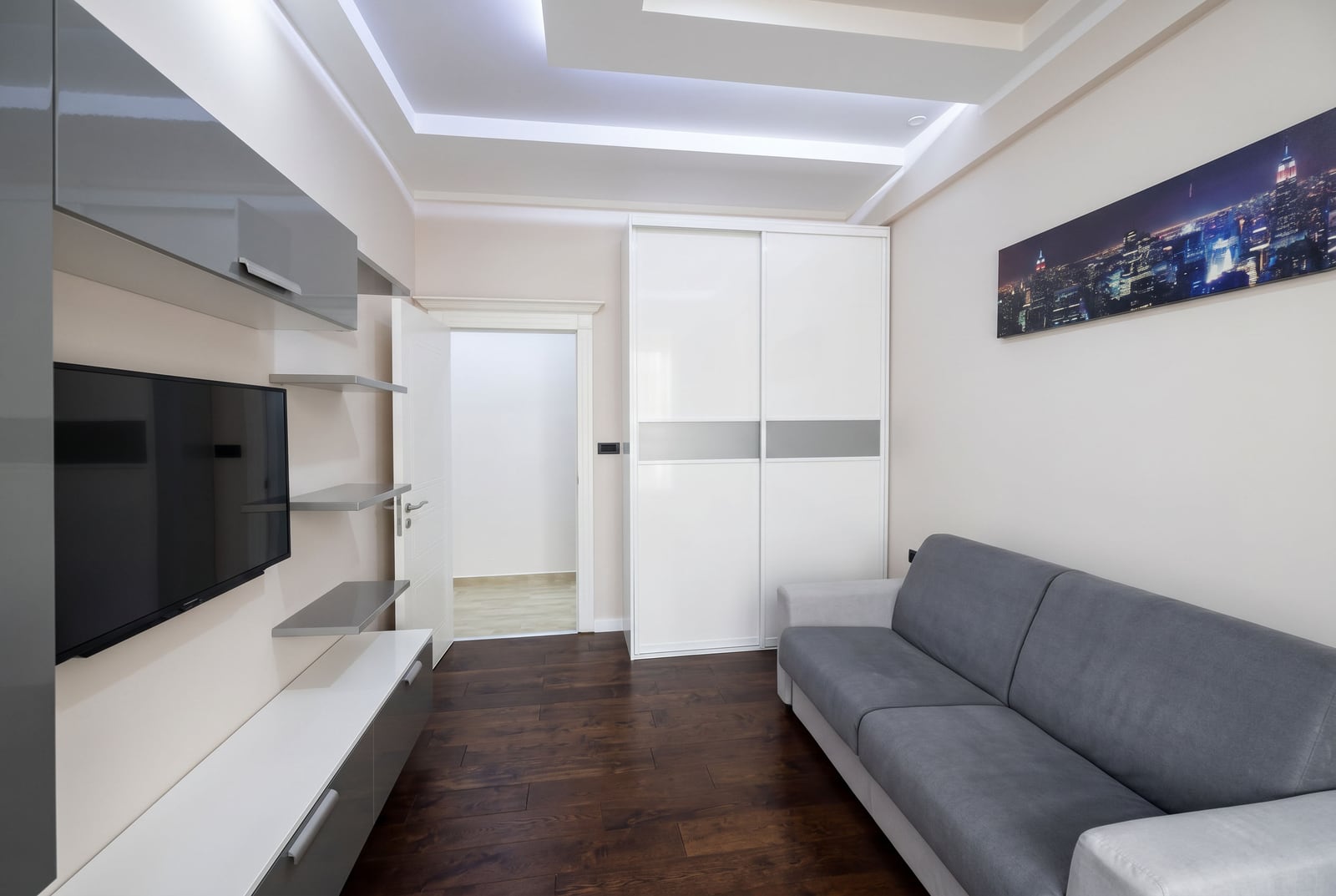 Modern living room with a grey sofa, TV area, and white sliding-door wardrobe in an apartment, Budva, Montenegro.