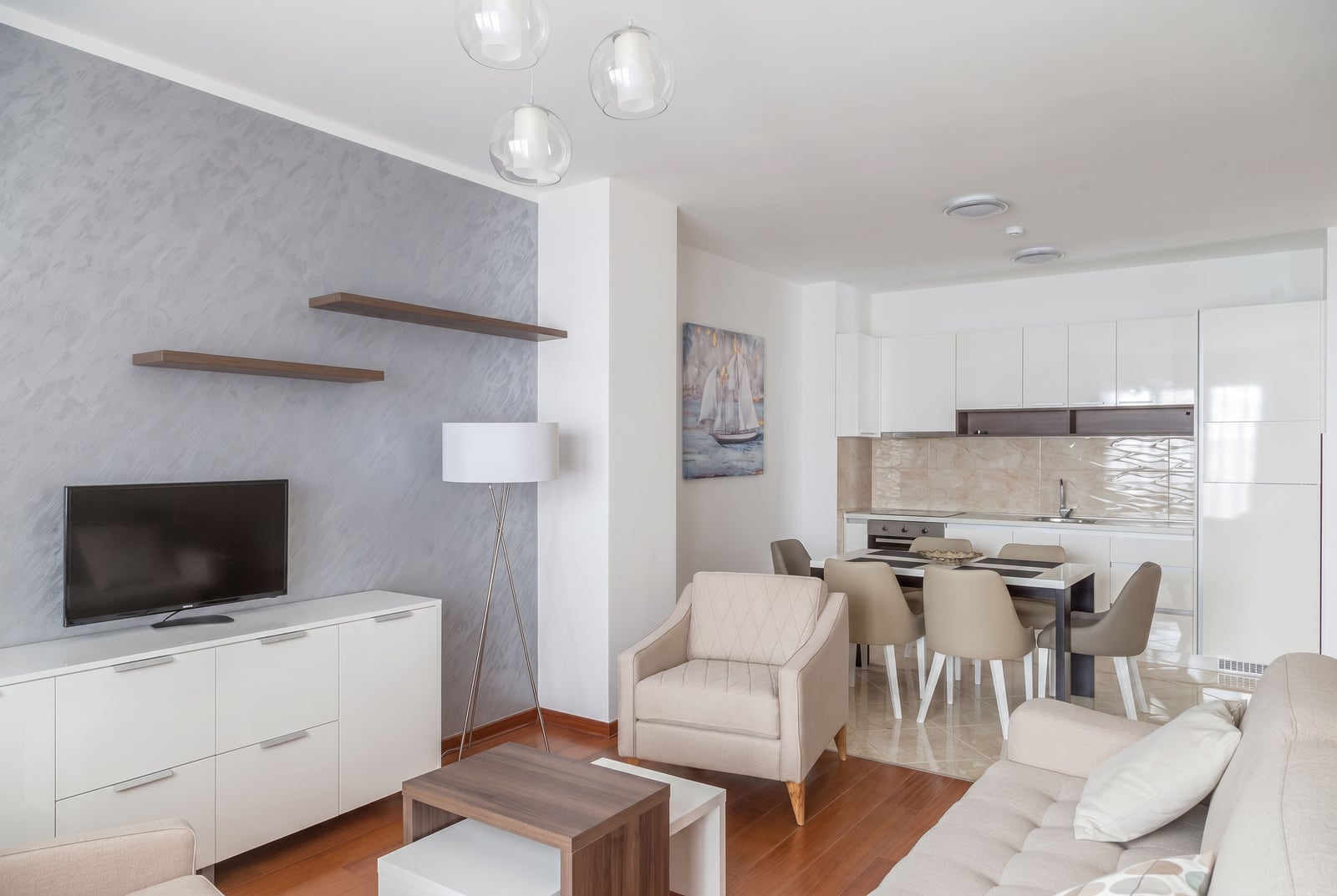Modern living room with a kitchen in an apartment in Becici, Montenegro: light-colored furniture, parquet flooring, and stylish wall finishes.