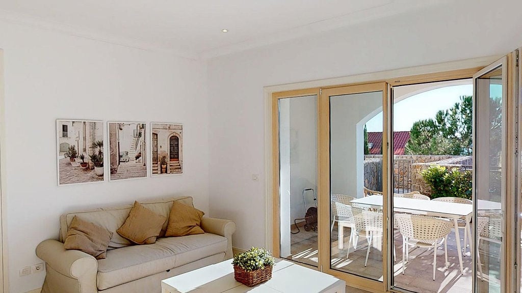 Bright living room with terrace access in an apartment, Luštica, Montenegro: beige sofa, panoramic windows, and garden view.