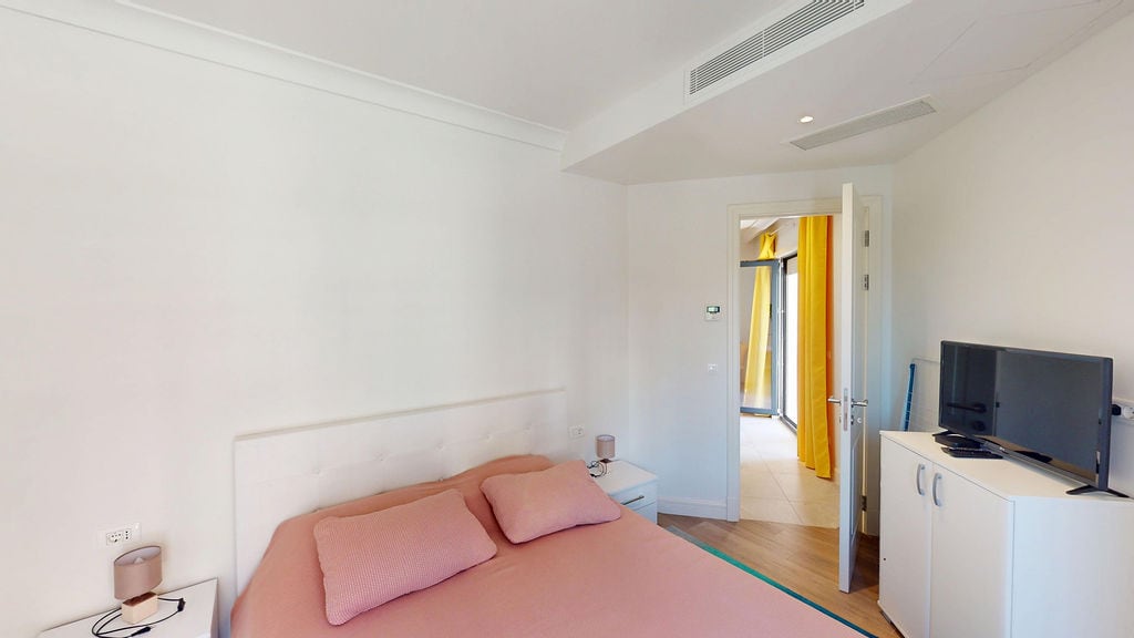 Bright bedroom with a double bed and TV in an apartment, Luštica Bay, Montenegro. Modern interior with balcony access.