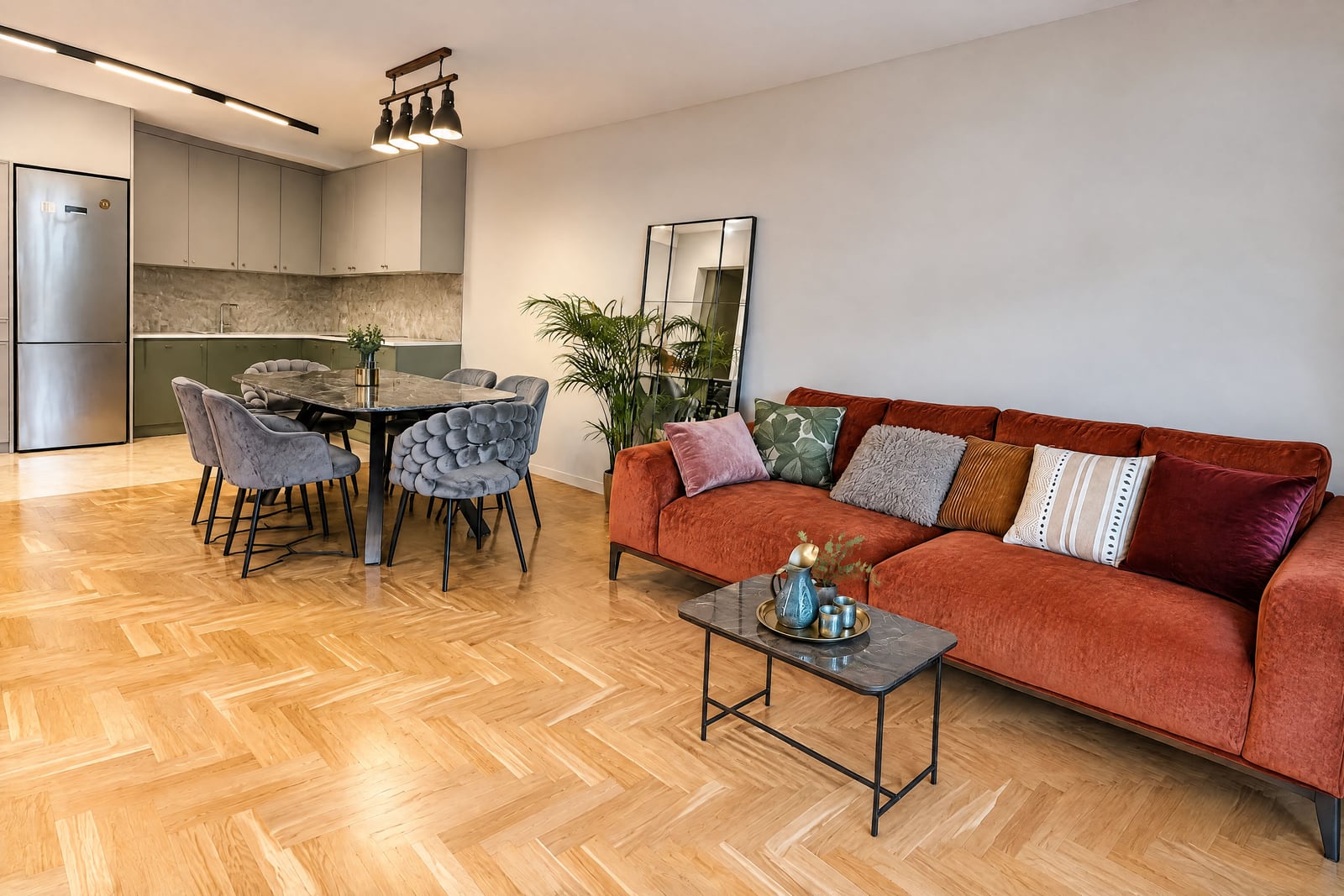 Living room with orange sofa, dining area, and open kitchen on parquet flooring.