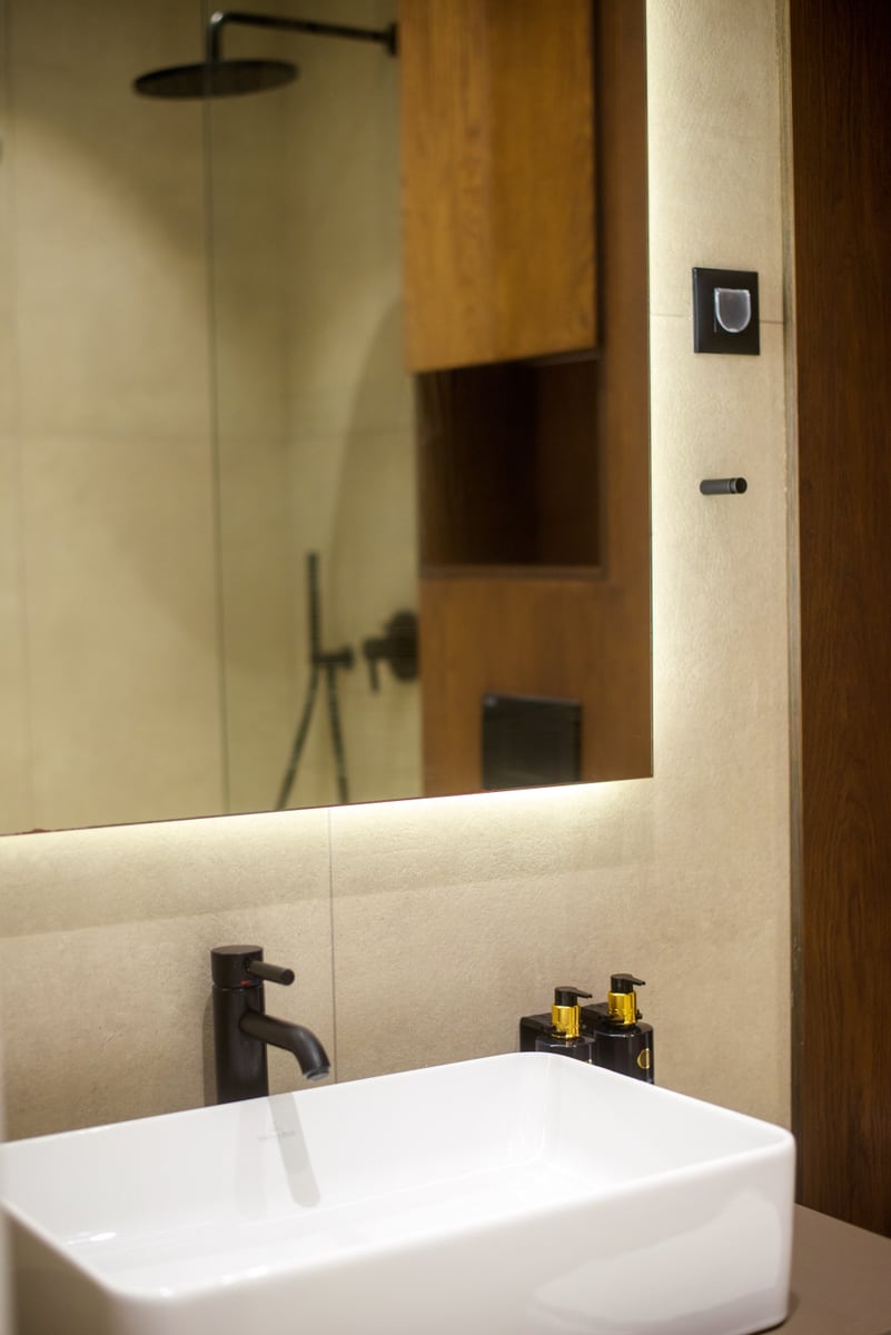 Modern bathroom in an apartment in Bečići, Montenegro: countertop sink, black fixtures, and a backlit mirror.