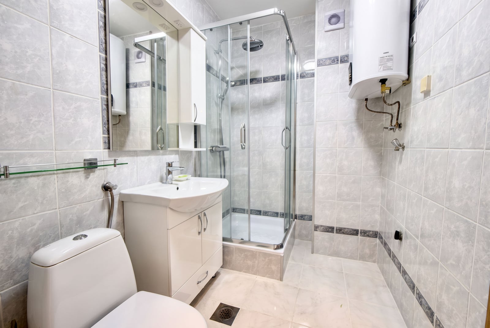 Bathroom in an apartment in Sveti Stefan, Montenegro: shower cabin, white vanity with sink, and water heater on the wall.