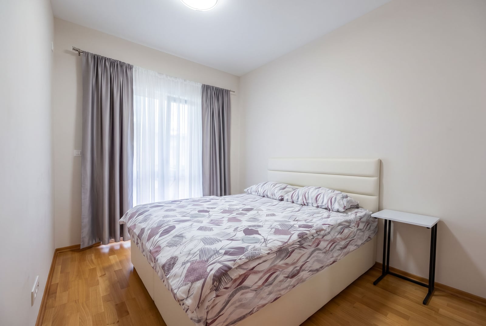 Bedroom featuring a double bed with white headboard, grey curtains, and wooden flooring.