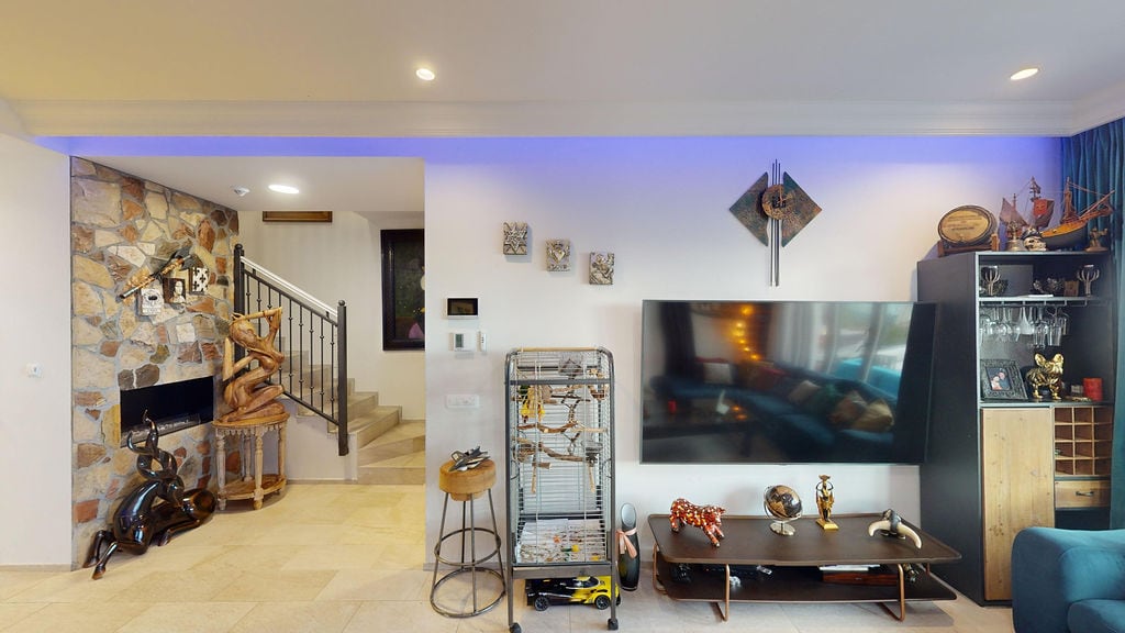 Living room in a townhouse in Luštica, Montenegro: stone wall cladding, fireplace, staircase, and a modern TV area.
