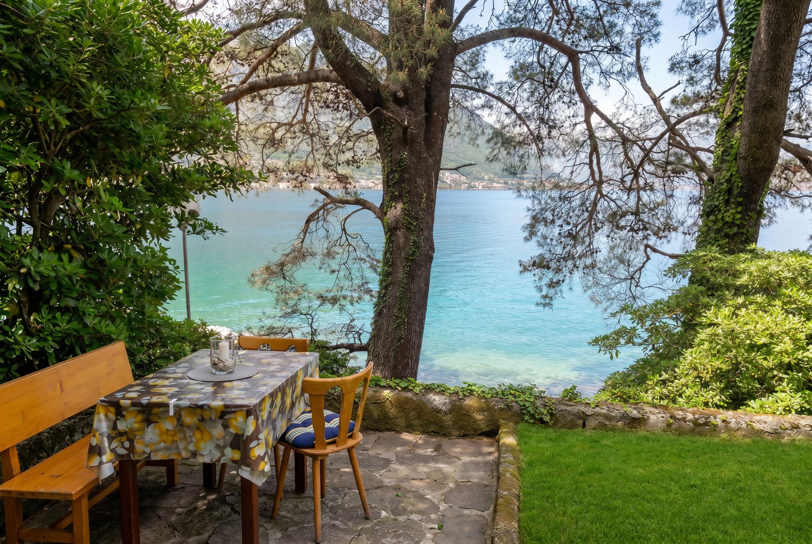 Terrace with a sea view in Dobrota, Montenegro: stone patio, wooden table, and a garden by the water.