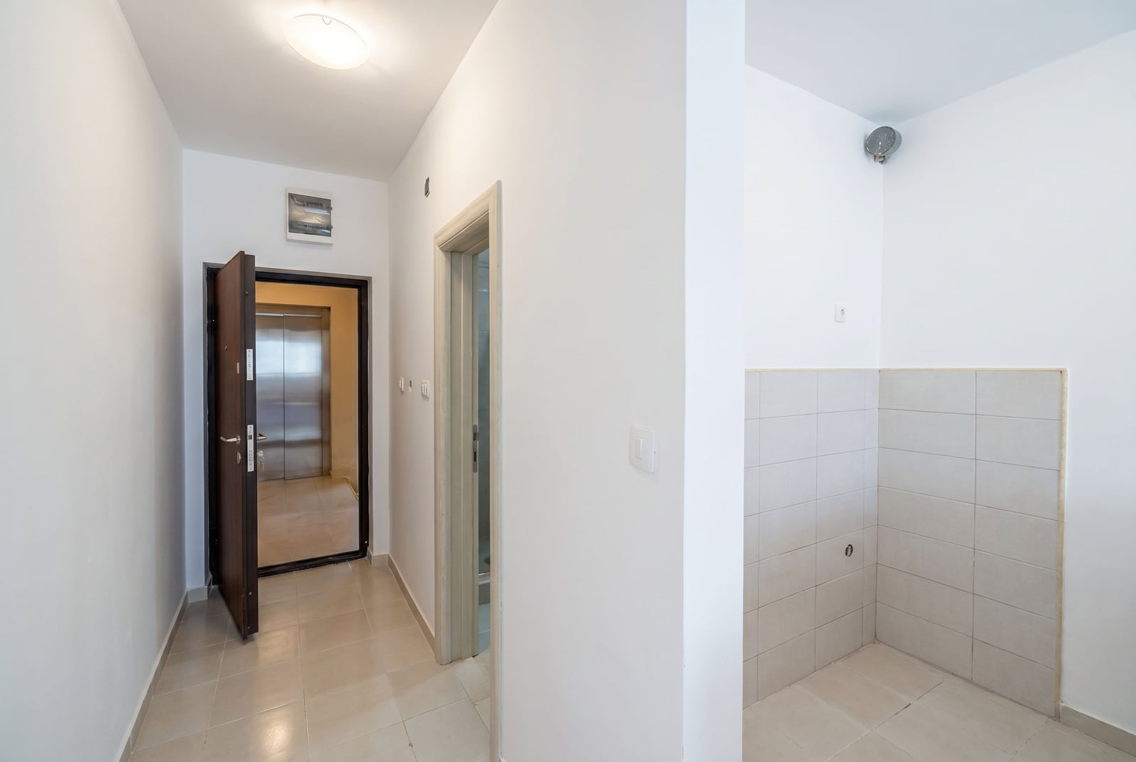 Entrance hall with tiled flooring and front door in an apartment, Budva, Montenegro. View of the elevator and kitchen area.