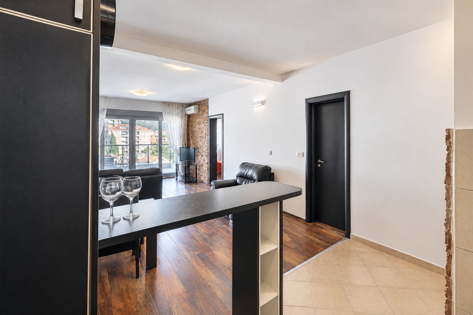 Living room featuring a black bar counter with wine glasses, leather sofa, TV, and exposed stone wall accent.