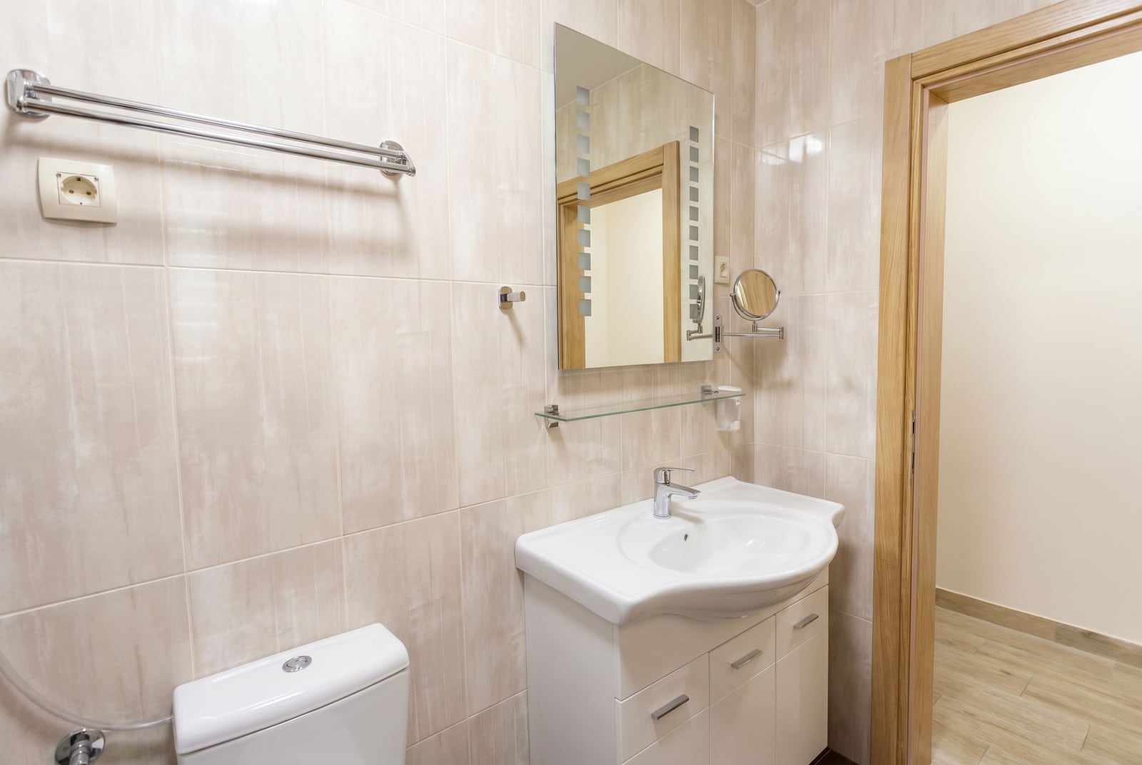 Bright bathroom in an apartment in Becici, Montenegro: white vanity with a sink, mirror, and beige tiles.