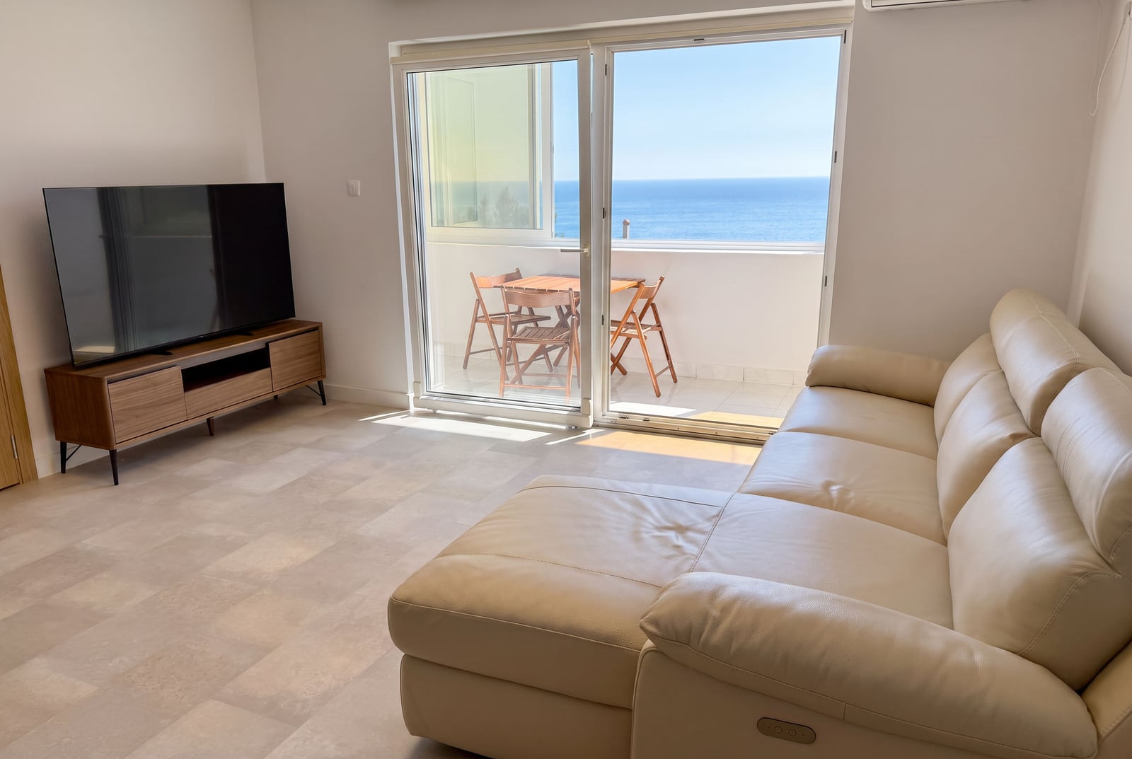 Living room in an apartment in Sveti Stefan, Montenegro: bright interior, leather sofa, TV area, and balcony with sea view.