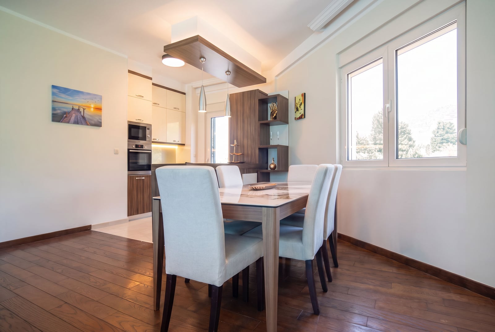 Modern kitchen with dining area, wood flooring, built-in appliances, and pendant lights.