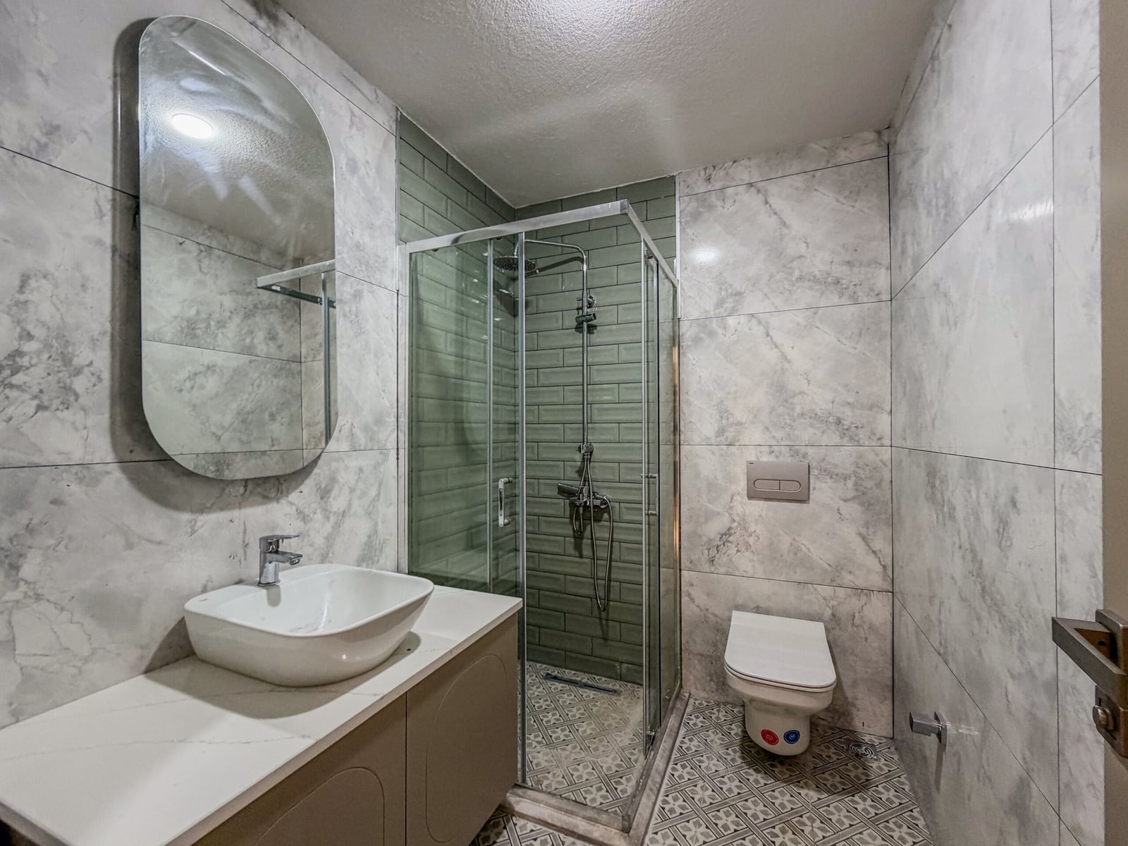 Bathroom featuring a glass shower stall, vessel sink on a vanity, and toilet against marble tiles.