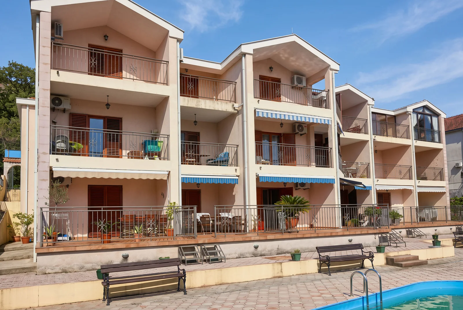 Exterior view of a multi-story building with balconies, a terrace, and a pool edge in the foreground.