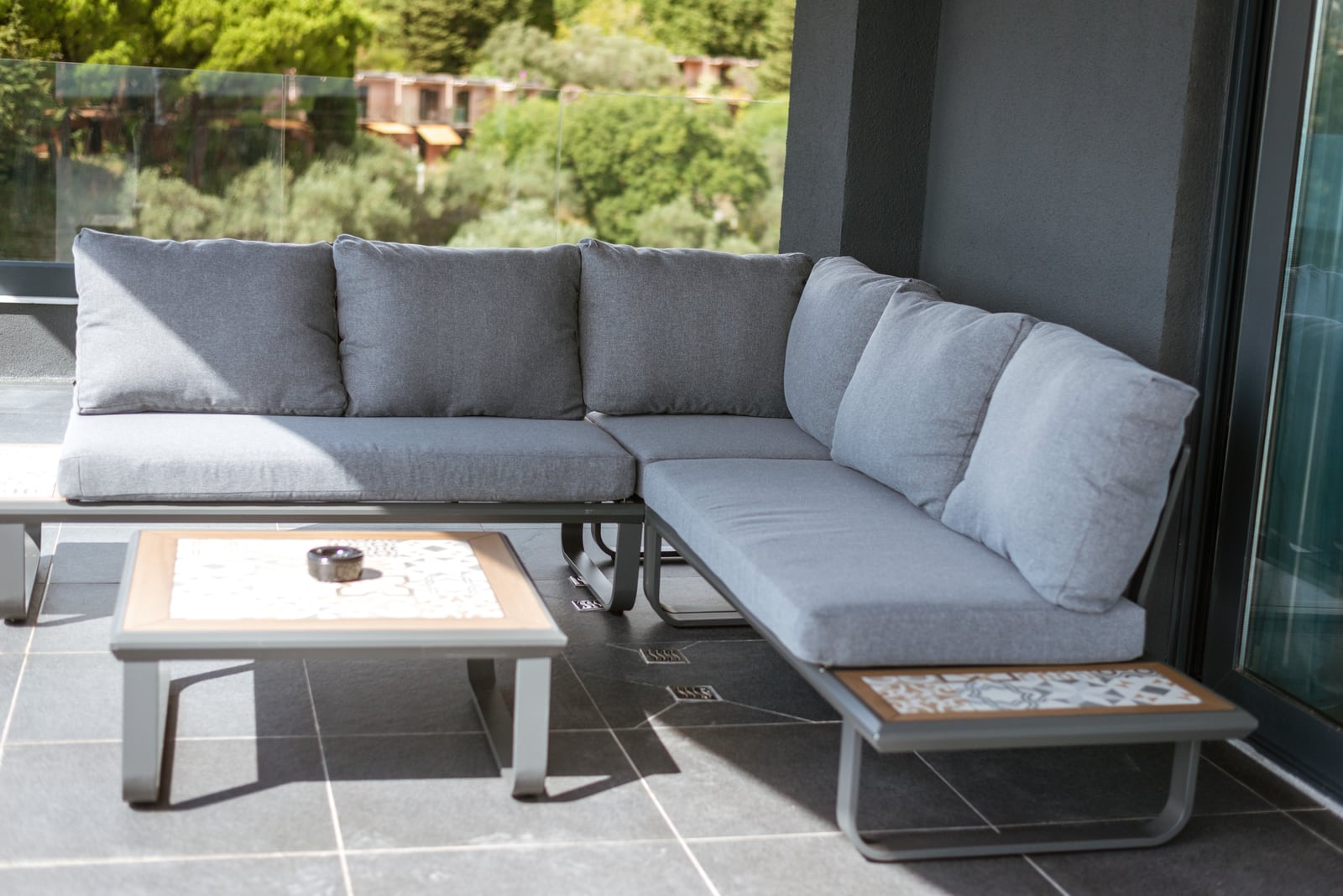 Corner sofa with gray cushions on the terrace of an apartment in Bečići, Montenegro, overlooking a green landscape.