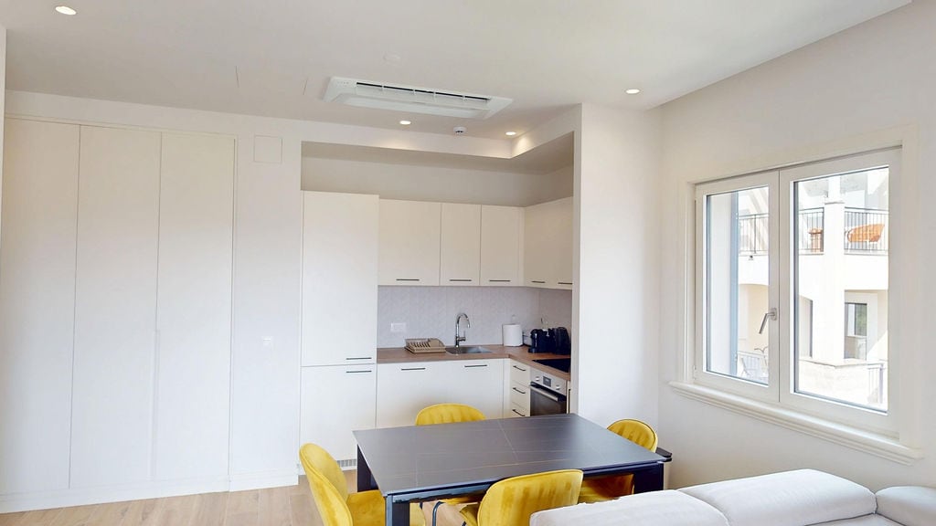 Modern kitchen-living room with white cabinetry and yellow chairs in the Lustica Bay apartments, Luštica, Montenegro.