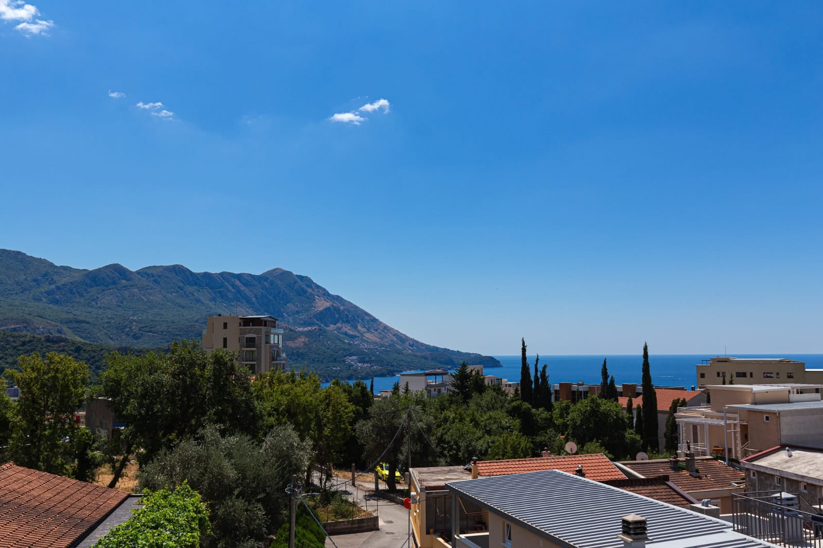 Panoramic view of the sea and mountains from a villa terrace in Becici, Montenegro: a picturesque landscape with rooftops and greenery.