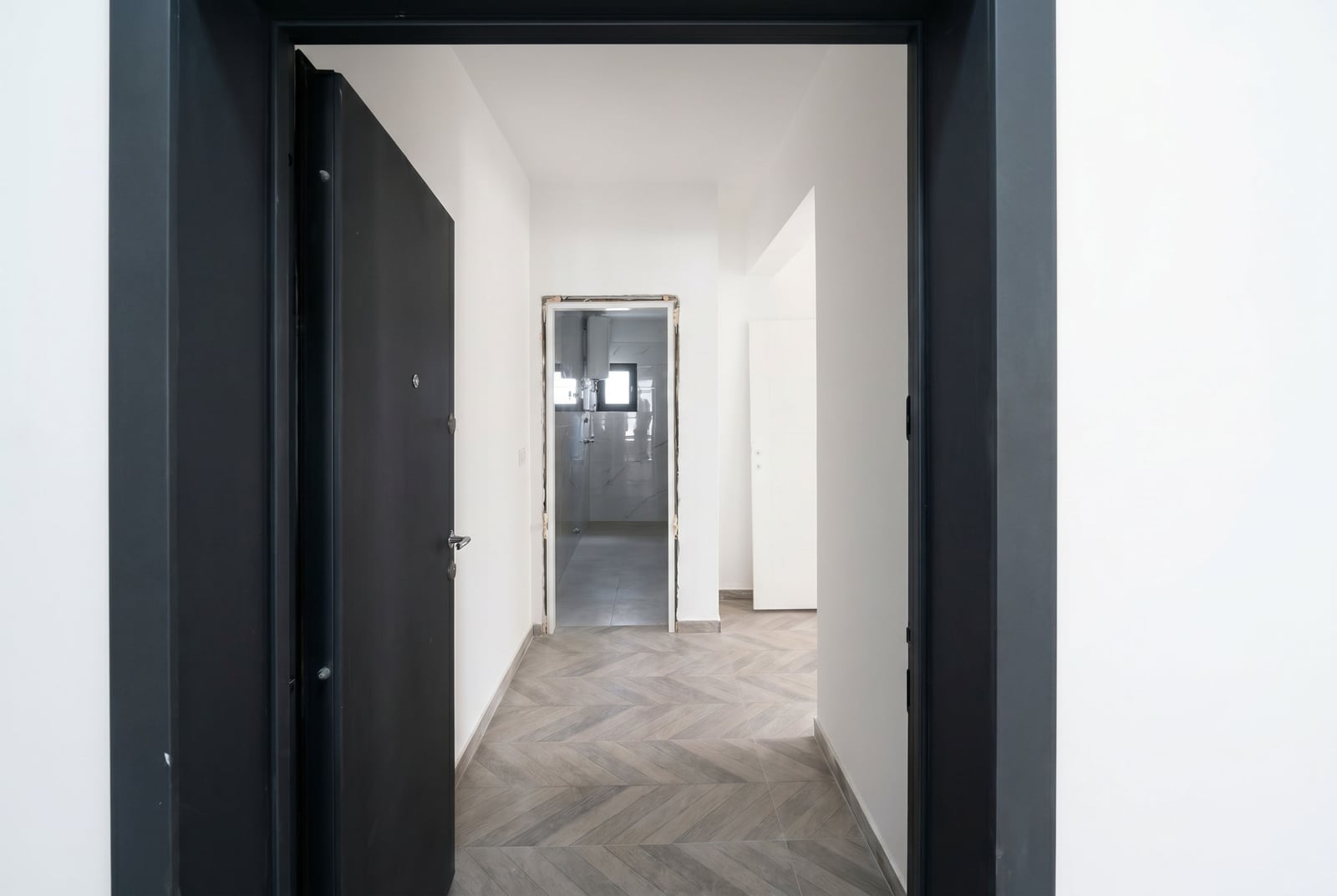 Entrance hall in a new apartment in Budva, Montenegro: light-toned finishes, herringbone flooring, and contrasting black doors.