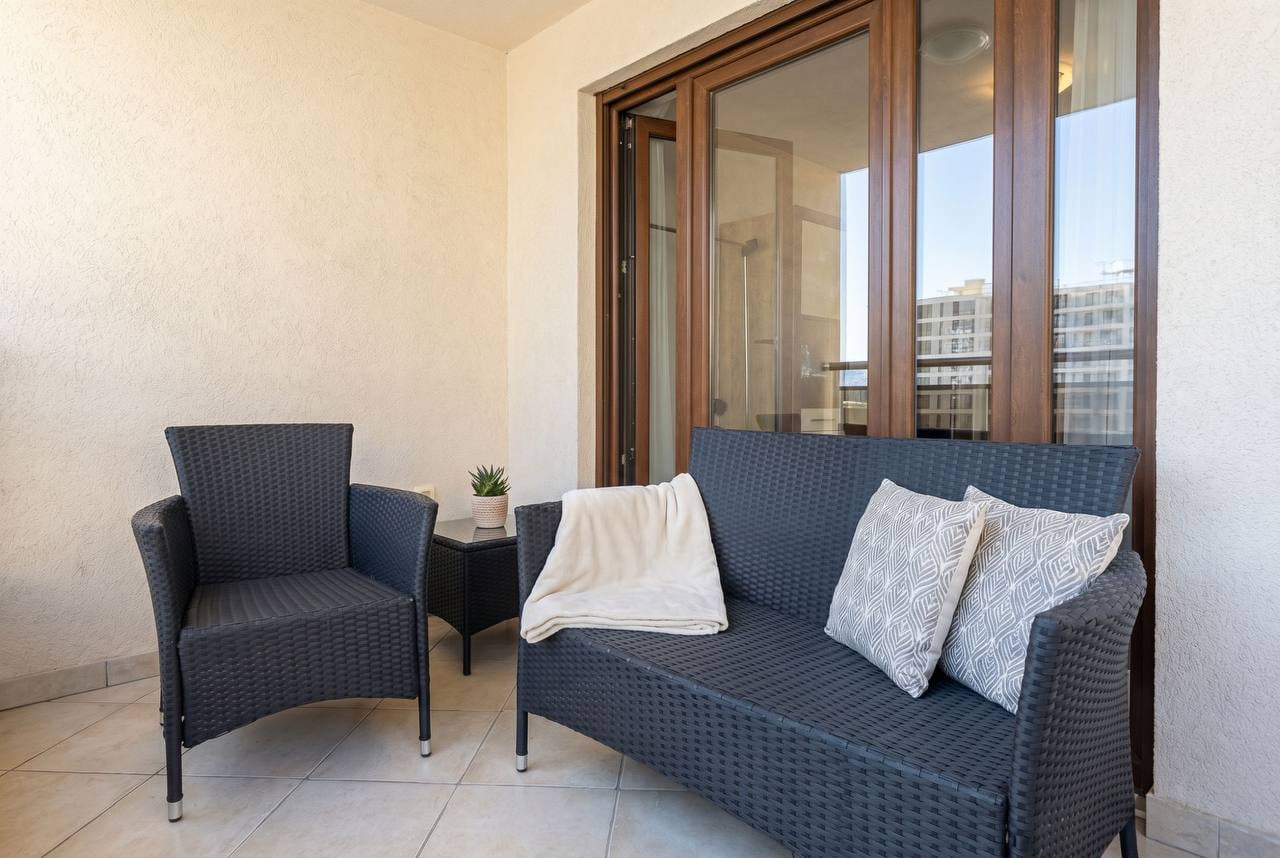 Cozy balcony with wicker furniture in an apartment in Budva, Montenegro: sofa, armchair, and panoramic glazing.